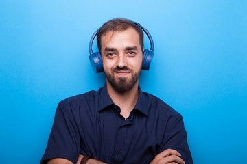 Young man listening to music through headphones on blue background 