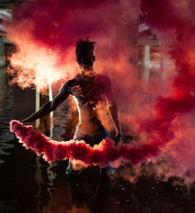 Young African man stands under bridge and holds colored red smoke bomb in his hands.
