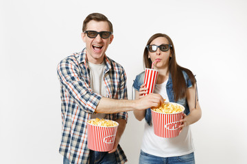 Young laughing couple, woman and man in 3d glasses watching movie film on date holding bucket of popcorn, plastic cup of soda or cola stealing popcorn isolated on white background. Emotions in cinema.