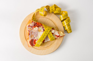 Piece of pizza wrapped in a measuring tape lies on a round wooden board on a white background. Top view.