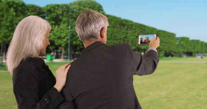 Mature couple in Paris looking at picture on their smartphone, Happy male and female tourists using mobile phone outdoors, 4k