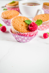 Sweet summer dessert, homemade baked muffin with raspberry jam, served with tea, fresh raspberries and mint. On a white marble table, copy space