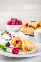 Sweet summer dessert, homemade baked mini croissants with berry jam, served with tea, fresh raspberries, blueberries and mint. On a white marble table, copy space