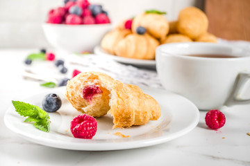 Sweet summer dessert, homemade baked mini croissants with berry jam, served with tea, fresh raspberries, blueberries and mint. On a white marble table, copy space