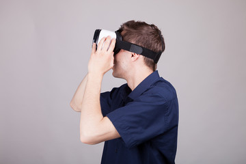 Young man wearing a VR headset on gray background in studio photo. He is experiencing virtual reality for the firts time and it is very happy