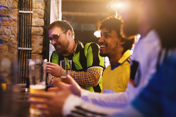 Cheerful football fans have gathered in their favorite pub to drink beer and watch an important...