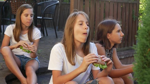 Triple sisters twins teen girls sitting on backyard porch terrace eating sandwiches