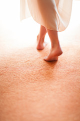 young woman's feet close up, walking on tiptoe on a soft carpet floor, into window light