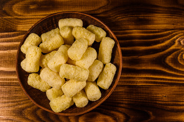 Ceramic plate with corn sticks on wooden table. Top view