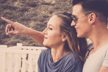 nice beuaitufl caucasian couple smile and look in front of them. the young man show the lady something far. summer day with sunlight. vintage colors filter. nice people outdoor on the terrace