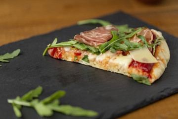 Slices of pizza with prosciutto, arugula and olives, on a black Board
