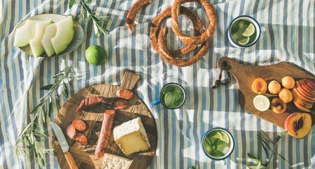 Wall murals Picnic Flat-lay of summer picnic set with fruit, cheese, sausage, bagels and lemonade over striped blanket, top view