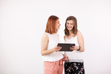 Happy female friends looking at a tablet PC over a white wall in studio photo