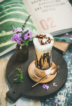 Iced mocha coffee with whipped cream, ice cream and chocolate sauce, served in tall glass on wooden board over rustic textured background. Summer beverage concept