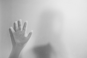 Shadow hands of the woman behind frosted glass.Blurry hand abstraction.Halloween background.Black and white picture.
