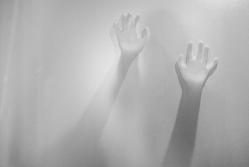 Shadow hands of the woman behind frosted glass.Blurry hand abstraction.Halloween background.Black and white picture.