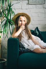 Cute little girl is lying on the green sofa\couch indoor plants around. Summer vacation begins. Vertical orientation