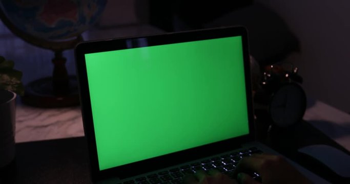 Laptop with green screen. Dark office. Dolly in . Perfect to put your own image or video.Green screen of technology being used. Chroma Key laptop
