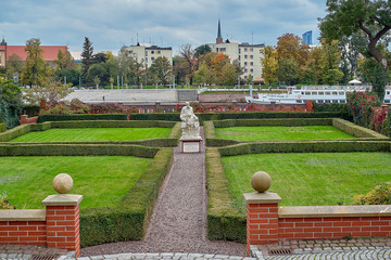 Gardens of The Archbishops Palace near Collegiate church of the Holy cross and St Bartholomew in Ostrow Tumski, Wroclaw, Poland. View to the Oder (Odra) river with Bulwar Xawerego Dunikowskiego. - obrazy, fototapety, plakaty