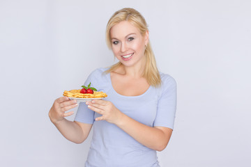 A happy blonde is holding a plate with Belgian waffles in her hands. Breakfast is decorated with strawberries and mint leaves. Concept: home food.
