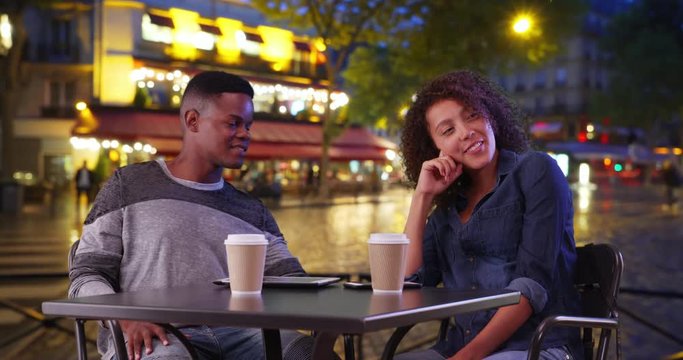 African American man and woman meeting for coffee on Paris street at night, Smiling black male and female enjoy their evening drinking coffee and chatting, 4k