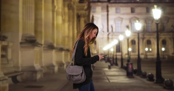 Pretty Caucasian woman on Paris street at night looking around, Young woman using app on smartphone for directions, 4k