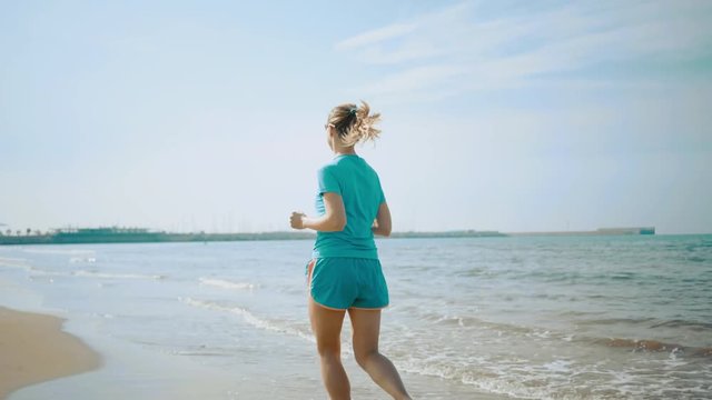 Running woman. Runner is jogging in sunny day light in the sea background. Female fitness training outdoors on summer day, 4K