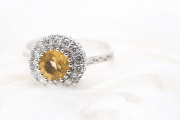 Yellow gem stone and diamond ring on white fabric