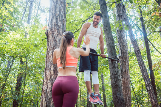 Woman watches man doing exercises on high bars in forest gym