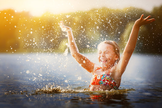 little girl playing in the river. A girl with blond hair raises her hands up in the water and splashes water drops