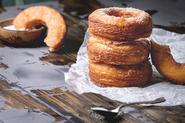 Homemade puff pastry deep fried donuts or cronuts in stack with sugar standing on crumpled paper over dark wooden concrete table.
