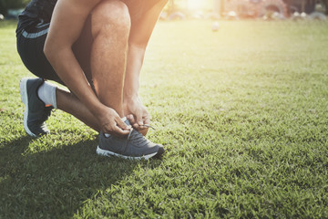 runner tying shoelace on grass at park with sunset