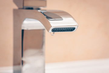 A drop hangs on the faucet in the bathroom, saving natural resources, saving water