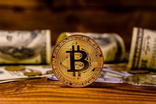 Bitcoins and one hundred dollar bills on wooden table