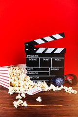 Film watching. Popcorn, clapperboard and glasses on wooden and red background