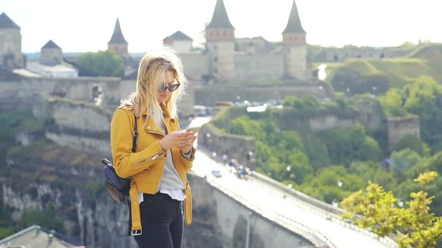 woman tourist using smart phone mobile for making selfie photo with old ancient brick castle on background beautiful sunny day female photography historic city center traveling concept trendy blogging