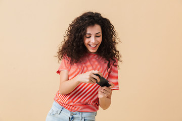 Emotional excited young curly woman play games by mobile phone.