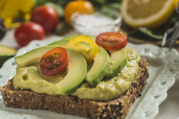 Green Avocado Spread and Organic Slices with Fresh Cherry Tomato as Vegan Breakfast Concept