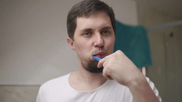 Close up shot of a handsome man with beard brushing his teeth in a bathroom in the morning. Standing in fornt of a mirror. Morning hygiene.