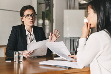 Photo of strict caucasian woman holding resume, and negotiating with female candidate during...