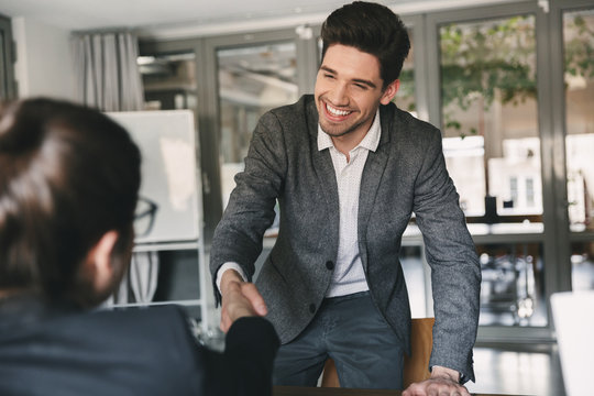 Business, career and placement concept - joyful young man 30s smiling and shaking hands with businesswoman, when was recruited during interview in office