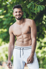 happy shirtless young man looking at camera in front of green leaves