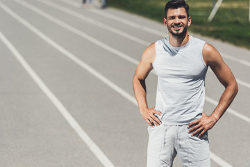 smiling young sporty man standing on running track with arms akimbo