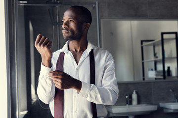 thoughtful young businessman in white shirt buttoning cufflinks and looking away