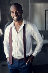 smiling young businessman in white shirt with tie hanging on shoulders at bathroom