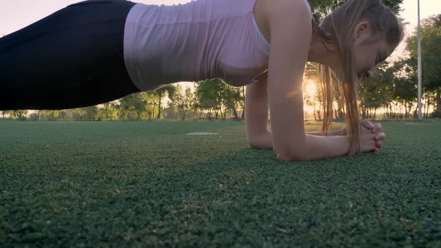 Two young womans doing plank exercise on field in park during sunset, fitness models exercising