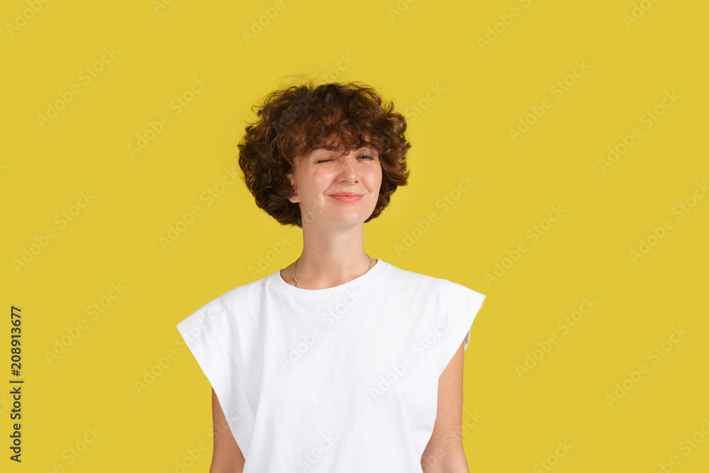 Wall mural funny shaggy hairstyle female teenager wearing casual white t-shirt having joyful expression blinkin