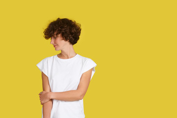 Indoor isolated shot of beautiful stylish woman with shaggy haircut wearing oversize white t-shirt and posing at yellow studio wall with copy space for your advertising concept. Look aside. Youth