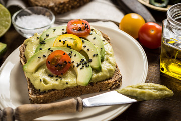 Avocado Spread and Slices with Cherry Tomato and Black Sesame on Wooden Background as Vegetarian Food Concept