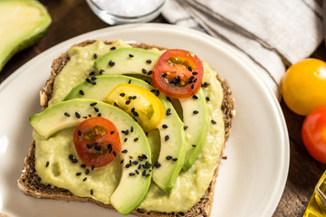 Avocado Spread and Slices with Cherry Tomato and Black Sesame on Wooden Background as Vegetarian Food Concept